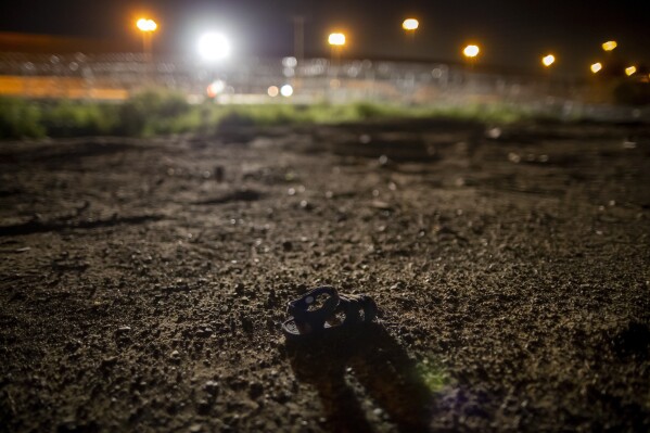 An abandoned baby sandal lies on the banks of the Rio Grande in Ciudad Juarez, Mexico with the razor wire and border wall of El Paso, Texas, in the background, late Thursday, Aug. 8, 2024. (AP Photo/Andres Leighton)