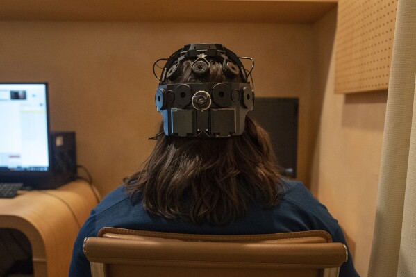 Emily Hollenbeck, a deep brain stimulation therapy patient, demonstrates an EEG device that records brain activity as she reacts to short videos at Mount Sinai’s “Q-Lab” in New York on Dec. 20, 2023. Dr. Brian Kopell, who directs Mount Sinai's Center for Neuromodulation, says in normal brains electrical activity reverberates unimpeded in all areas, in a sort of dance. In depression, the dancers get stuck within the brain’s emotional circuitry. DBS seems to “unstick the circuit,” he says, allowing the brain to do what it normally would. (AP Photo/Mary Conlon)