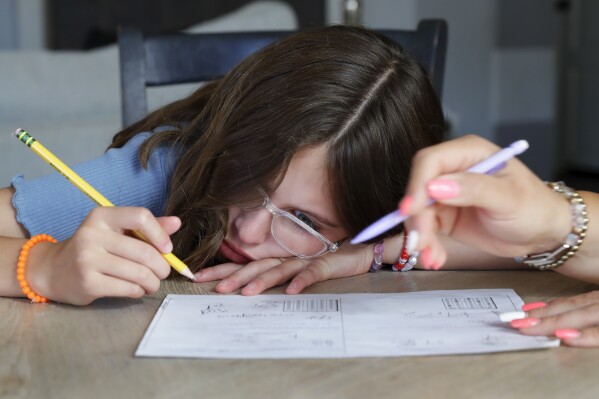 Giada Gambino, 10, left, becomes frustrated with a problem on a math worksheet from school as her mother helps her work through it at the dining room table in their home Wednesday, Aug. 23, 2023, in Spring, Texas. (AP Photo/Michael Wyke)