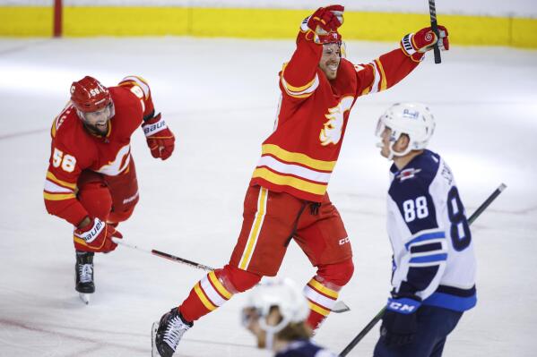 Winnipeg Jets' Nate Schmidt, lower right, skates away as Calgary Flames' Elias Lindholm, top right, celebrates his winning goal while Flames' Oliver Kylington, left, looks on during third-period NHL hockey game action in Calgary, Alberta, Monday, Feb. 21, 2022. (Jeff McIntosh/The Canadian Press via AP)