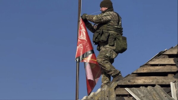 In this photo distributed by the Russian Defense Ministry Press Service on Monday, March 17, 2025, a Russian soldier prepares to raise a flag atop a house in Staraya Sorochina, a village in the Sudzha district of the Kursk region of Russia after it was taken over by Russian troops. (Russian Defense Ministry Press Service via AP)