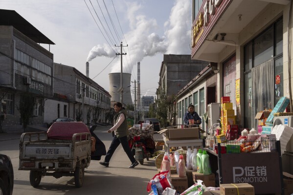 Guohua Power Station, a coal-fired power plant, operates as people sell items on a street in Dingzhou, Baoding, in the northern China's Hebei province, Friday, Nov. 10, 2023. (AP Photo/Ng Han Guan)