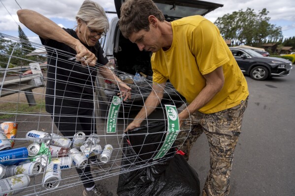 Paula Ambre, a volunteer at the Kula distribution hub, puts recycled bottles and cans into a trash bag with Kyle Ellison on Wednesday, Sept. 27, 2023, in Kula, Hawaii. Ellison collects the water bottles and cans and puts the money toward rebuilding the community, such as by renting wood chippers. (AP Photo/Mengshin Lin)