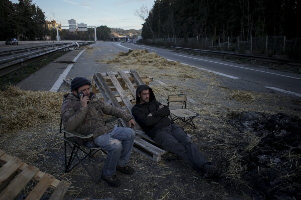 FILE - Farmers sit on a highway after spending the night barricaded in Aix-en-Provence, southern France, Tuesday, Jan. 30, 2024. Protesting farmers in France have surrounded Paris with tractor barricades and declared a 