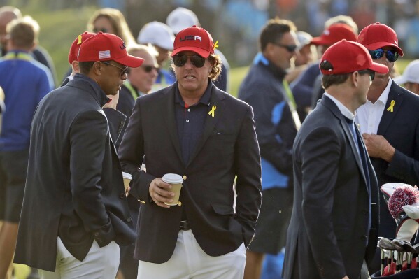 FILE - Tiger Woods, left, and Phil Mickelson wait for the closing ceremony after Europe won the Ryder Cup on the final day of the 42nd Ryder Cup at Le Golf National in Saint-Quentin-en-Yvelines, France, Sept. 30, 2018. It was the sixth straight road loss in the Ryder Cup for the Americans. (AP Photo/Matt Dunha, File)