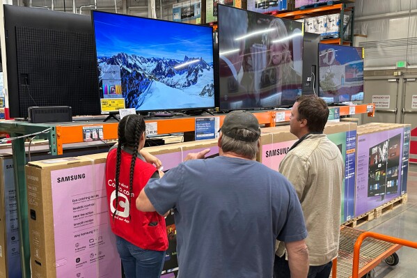 Shoppers consider a large-screen television with the help of a sales associate in a Costco warehouse Thursday, May 1, 2025, in Sheridan, Colo. (AP Photo/David Zalubowski)