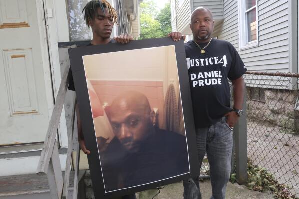 FILE - Joe Prude, brother of Daniel Prude, right, and his son Armin, stand with a picture of Daniel Prude in Rochester, N.Y., on Thursday, Sept. 3, 2020. One of several police officers seen on video pinning down Prude, a Black man who died after being detained on a street in upstate New York, faces potential departmental discipline, the Rochester Police Department said. Officer Mark Vaughn is the only officer to be served with "departmental charges" Thursday following an internal investigation of the police response to Prude, whose death sparked nightly protests and led to the suspension of seven officers. (AP Photo/Ted Shaffrey, File)