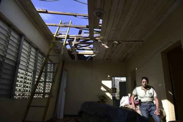 In this Nov. 15, 2017 photo, Edgardo de León sits in his living room with a hole in the ceiling caused by the whip of hurricane Maria, in Cataño, Puerto Rico.   A newly created Florida company with an unproven record won more than $30 million in contracts from the Federal Emergency Management Agency to provide emergency tarps and plastic sheeting for repairs to hurricane victims in Puerto Rico. Bronze Star LLC never delivered those urgently needed supplies, which even months later remain in demand on the island.  (AP Photo/Carlos Giusti)