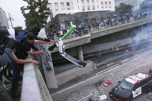 A protester throws a scooter at a police vehical near the metropolitan detention center of downtown Los Angeles, Sunday, June 8, 2025, following last night's immigration raid protest. (AP Photo/Jae C. Hong)