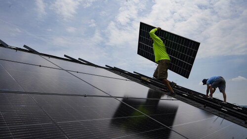 Nicholas Hartnett, owner of Pure Power Solar, carries a panel as he and Brian Hoeppner, right, install a solar array on the roof of a home in Frankfort, Ky., Monday, July 17, 2023. Since passage of the Inflation Reduction Act, it has boosted the U.S. transition to renewable energy, accelerated green domestic manufacturing, and made it more affordable for consumers to make climate-friendly purchases, such as installing solar panels on their roofs. (AP Photo/Michael Conroy)