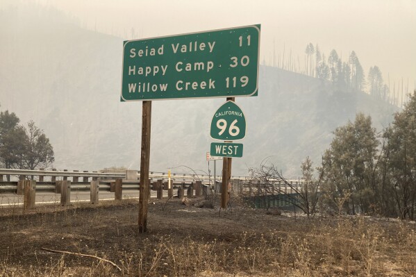 In this photo provided by Caltrans, smoke from the Head Fire blankets the closed State Route 96 in Klamath National Forest, Calif., on Wednesday, Aug. 16, 2023. Rural areas near California's border with Oregon were under evacuation orders Wednesday after gusty winds from a thunderstorm sent a lightning-sparked wildfire racing through national forest lands, authorities said. The blaze in Siskiyou County was one of at least 20 fires that erupted as thunderstorms brought lightning and downdrafts that drove the flames through timber and rural lands. (Billy Shakespeare/Caltrans via AP)