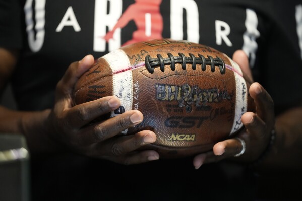 Phillip Laster Sr. holds a football in Brandon, Miss., Tuesday, Aug. 27, 2024, signed by teammates of his son Phillip Laster Jr., that was given to him on senior night after his passing. (AP Photo/Gerald Herbert)