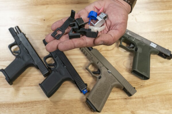 A handful of fully automatic conversion devices is displayed for a photograph, above semi-automatic pistols, some with conversion devices installed making them fully automatic, at the Bureau of Alcohol, Tobacco, Firearms, and Explosives (ATF), National Services Center, Thursday, March 2, 2023, in Martinsburg, W.Va. Machine guns have been illegal in the U.S. for decades, but in recent years the country has seen a new surge of weapons capable of automatic fire. Small pieces of plastic or metal used to convert legal guns into homemade machine guns are helping to fuel gun violence. (AP Photo/Alex Brandon)