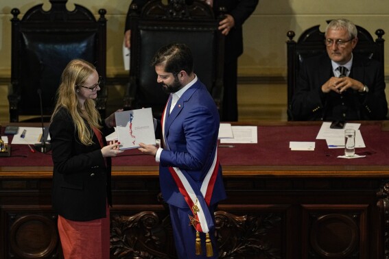Constitutional Council President Breatriz Hevia, left, presents Chilean President Gabriel Boric with the final draft of the new national Constitution by as Constitutional Council Vice President Aldo Valle looks on during a ceremony at the former National Congress building in Santiago, Chile, Tuesday, Nov. 7, 2023. Voters will decide on Dec. 17 to accept or reject the new Constitution. (AP Photo/Esteban Felix)