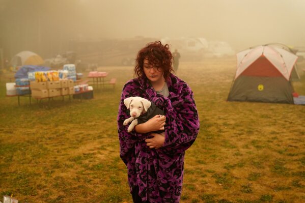 Shayanne Summers holds her dog Toph while wrapped in a blanket on Sept. 13, 2020, after staying several days in a tent at an evacuation center at the Milwaukie-Portland Elks Lodge in Oak Grove, Ore. Summers evacuated from near Molalla, Ore., which was threatened by the Riverside Fire. (AP Photo/John Locher)