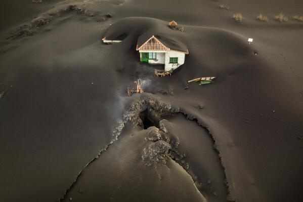 A fissure is seen next to a house covered with ash on the Canary island of La Palma, Spain, Wednesday, Dec.1 2021. A fissure that volcanologists believe spouted a gusher of lava left a gaping hole in front of house whose bottom floor was completely covered by a mountain of ash. A fresh stream of lava from volcano on Spain's La Palma threatened on Wednesday to engulf a parish church that has so far survived the eruption that shows no signs of relenting in its tenth week. (AP Photo/Emilio Morenatti)