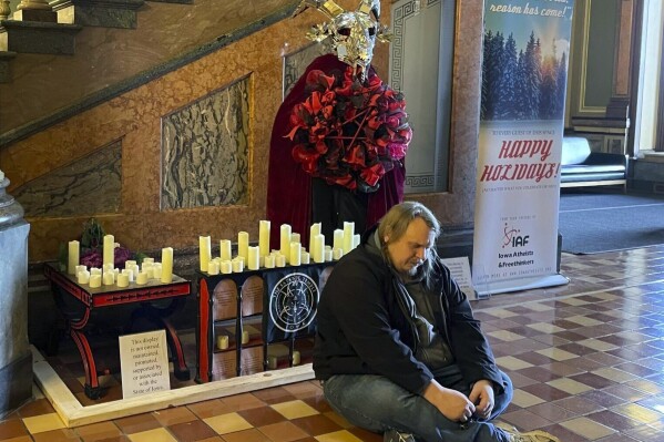 FILE - A man prays in Latin in front of a display installed by Satanic Temple Iowa at the Iowa State Capitol in Des Moines, Iowa, on Tuesday, Dec. 12, 2023. A Mississippi man accused of destroying a statue of the pagan idol Baphomet at Iowa's state Capitol pleaded guilty Friday to a reduced charge in return for prosecutors dropping a felony hate crime count. (Caleb McCullough/The Gazette via AP, file)