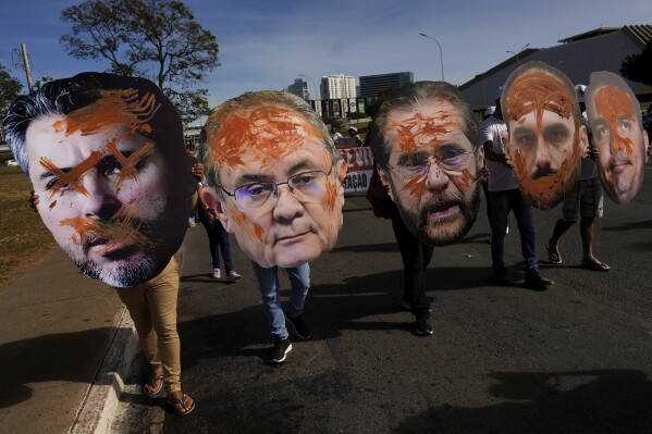 Varias personas cargan con los retratos de varios senadores durante una protesta ante el Congreso contra un proyecto de ley que cambiaría las leyes para licencias medioambientales, en el Día Mundial del Medio Ambiente, en Brasilia, Brasil, el 5 de junio de 2025. (AP Foto/Eraldo Peres)