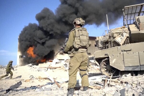 In this image taken from a video released by the Israeli Defense Forces on Tuesday, Nov. 14, 2023, an Israeli soldier holds a weapon in Gaza City. The Israeli military released footage on Tuesday that it said shows joint operational activity of two army brigades in its advancement on the ground in Gaza Strip. (Israel Defense Forces via AP)
