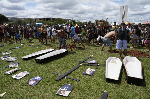 Indigenous people protest by digging holes for empty coffins symbolizing the death of lawmakers, who they say are against their rights and territorial protection, during a march at the annual Free Earth camp in Brasília, Brazil, Tuesday, April 8, 2025. (AP Photo/Eraldo Peres)