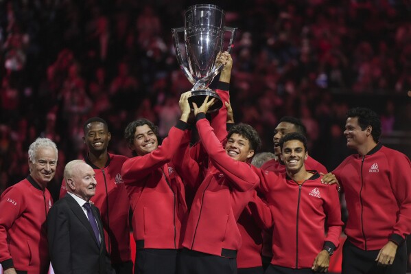 Team World's Taylor Fritz, fourth from left, and Ben Shelton, fifth from left, hoist the Laver Cup in front of teammates, John McEnroe, left, and Rod Laver, second from left, after Team World defeated Team Europe at the Laver Cup tennis tournament in Vancouver, British Columbia, Sunday, Sept. 24, 2023. (Darryl Dyck/The Canadian Press via AP)