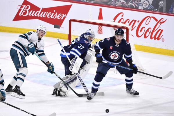 San Jose Sharks' Steven Lorentz (16), Winnipeg Jets goaltender Connor Hellebuyck (37) and Brenden Dillon keep their eyes on a bouncing puck during the third period of an NHL hockey game in Winnipeg, Manitoba, on Monday April 10, 2023. (Fred Greenslade/The Canadian Press via AP)