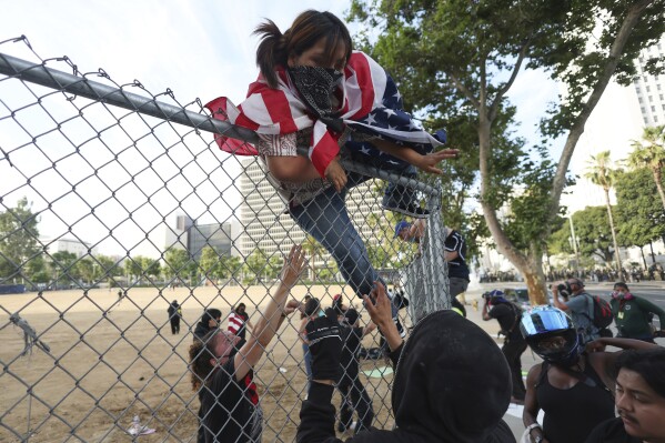 A woman climbs over a fence to escape a police kettle during a protest Saturday, June 14, 2025, in Los Angeles. (AP Photo/Ethan Swope)