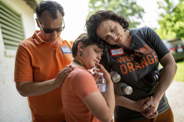 Hollan Holm, left, and his wife, Kate Dittmeier Holm, right, observe a moment of silence with their daughter, Sylvia, 11, during a rally against gun violence in Louisville, Ky., Saturday, June 3, 2023. Raising kids amid school shootings and neighborhood violence is enough to worry any parent. For those, like Hollan Holm who survived a school shooting during the Columbine era, it can be even harder. (AP Photo/David Goldman)