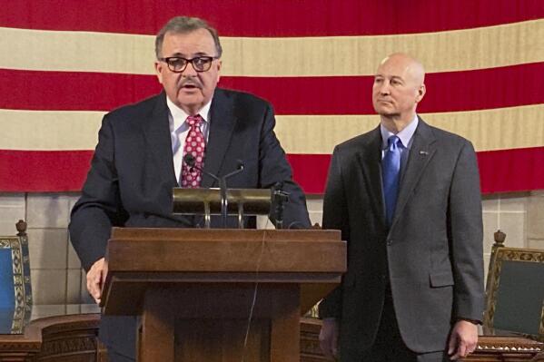 Newly appointed Nebraska state Sen. Mike Jacobson, left, of North Platte, addresses the media after being sworn into office following his appointment by Gov. Pete Ricketts, right, on Wednesday, Feb. 28, 2022, in Lincoln, Neb. Jacobson replaces former state Sen. Mike Groene, who resigned after admitting that he took photos of a legislative staffer without her knowledge. (AP Photo/Grant Schulte)