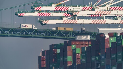 FILE - Transportation trucks cross the Vincent Thomas Bridge over the main channel as shipping containers are seen stacked on the Evergreen terminal at the Port of Los Angeles in San Pedro, Calif., Nov. 30, 2021. The union for thousands of West Coast dockworkers has reached a tentative agreement on a new contract, it was announced Wednesday, June 14, 2023, after more than a year of negotiations and several work disruptions that snarled shipping traffic at some of the largest ports. (AP Photo/Damian Dovarganes, File)