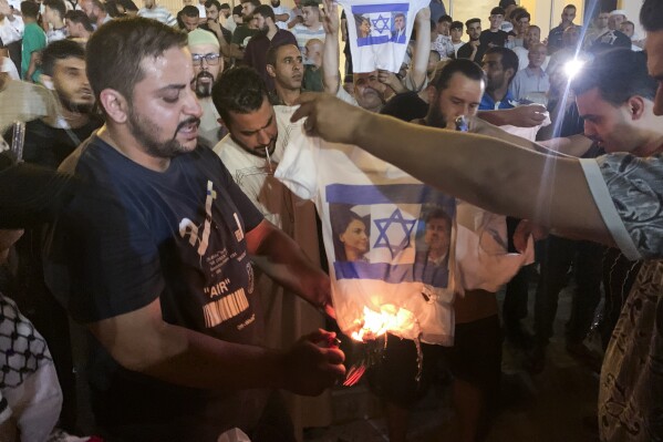 People burn a shirt showing Israeli Foreign Minister Eli Cohen and his Libyan counterpart Najla Mangoush in Tripoli, Libya, Sunday, Aug. 27, 2023. Cohen and Mangoush met in the Italian capital, Rome, last week, according to the Israeli foreign ministry. (AP Photo/Yousef Murad)