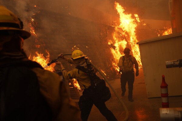 Firefighters protect structures from the advancing Palisades Fire in the Pacific Palisades neighborhood of Los Angeles, Tuesday, Jan. 7, 2025. (AP Photo/Etienne Laurent)