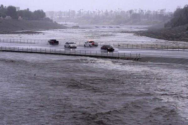 FILE - Vehicles cross over a flood control basin that has almost reached the roadway as Tropical Storm Hilary hits the area on Aug. 20, 2023, in Palm Desert, Calif. Former Hurricane Hilary was actually no longer a tropical storm but essentially had the same impact when its destructive remnants entered California last August, according to a new National Hurricane Center report. (AP Photo/Mark J. Terrill, File)