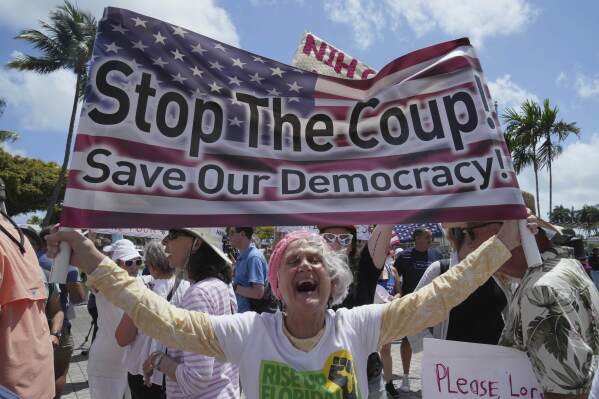 Protesters carry signs and chant slogans against the policies of President Donald Trump and Elon Musk Saturday, April 5, 2025, in Miami. (AP Photo/Marta Lavandier)