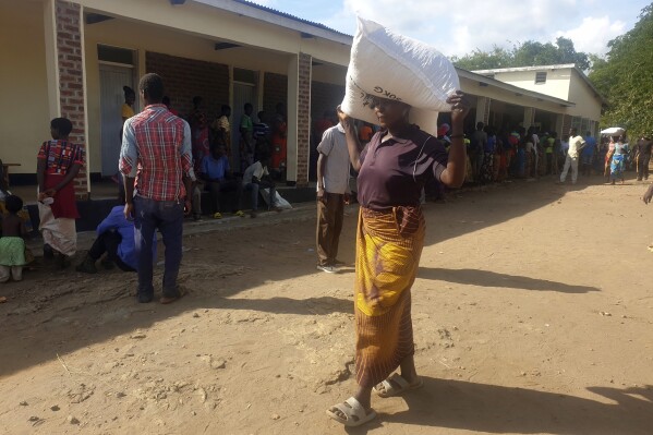 A woman carries a bag of maize meal received at a World Food Programme distribution center in Neno district southern Malawi. Sunday March 24, 2024. Malawi's President Lazarus Chakwera has declared a state of disaster over drought in 23 of its 28 districts saying the country urgently needs more than $200 million in humanitarian assistance. (AP Photo/Kenneth Jali).