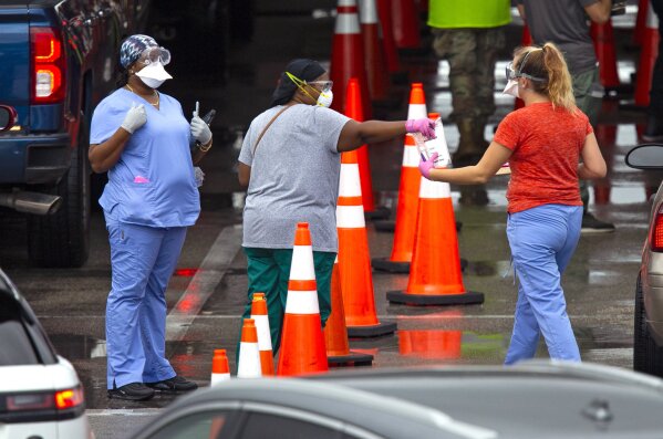 Vehicles line up as a healthcare workers help to check in as citizens is being tested at the COVID-19 drive-thru testing center at Hard Rock Stadium in Miami Gardens on Sunday, November 22, 2020.(David Santiago/Miami Herald via AP)