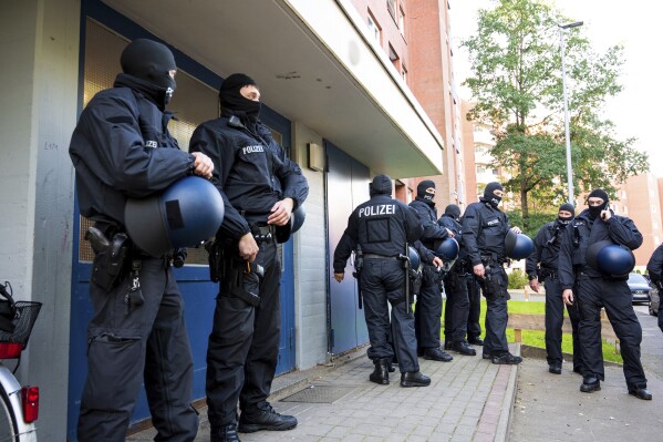 Police officers on duty during a raid stand in front of an apartment building in Stade, Germany, Tuesday Sept. 26, 2023. During a raid in five federal states, the federal police discovered several Syrians suspected of having been smuggled in early Tuesday morning. Arrest warrants had also been executed against suspected smugglers. (Daniel Bockwoldt/dpa via AP)