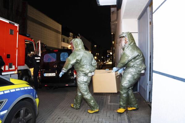Men in protective suits carry a cardboard box out of a house in Castrop-Rauxel during an anti-terror operation on Sunday, Jan. 8, 2023. German investigators are searching two garages used by an Iranian man arrested on suspicion that he could be planning an attack with deadly chemicals. The 32-year-old and his 25-year-old brother were detained on Saturday night in Castrop-Rauxel, in western Germany, following a tip from U.S. security officials. (7aktuell.de, Marc Gruber/dpa via AP)