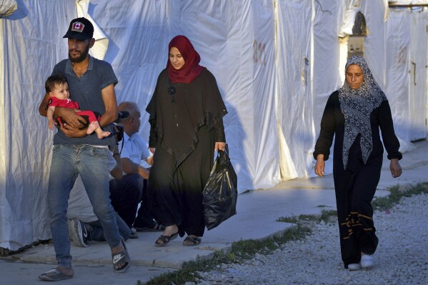FILE - Syrian refugee families walk back into a refugee camp after running errands in the town of Bar Elias, in the Bekaa Valley, Lebanon, July 7, 2022. Faced with an increasing funding crunch, the United Nations will cut the number of refugee families receiving cash assistance in Lebanon by nearly one-third next year, a spokesperson for the U.N. refugee agency said Thursday, Nov. 2, 2023. (AP Photo/Bilal Hussein, File)