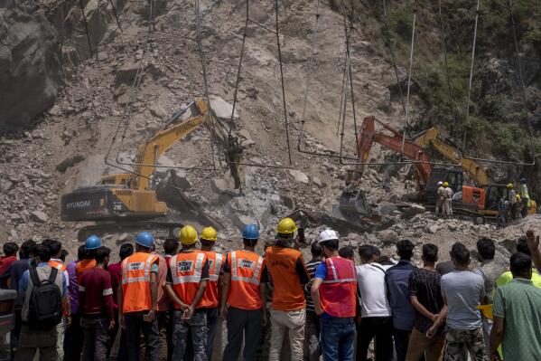 Rescue workers watch from a distance as earth movers dig through rubble of a collapsed tunnel in Ramban district, south of Srinagar, Indian controlled Kashmir, Friday, May 20, 2022. An official in Indian-controlled Kashmir said Friday that 10 workers were trapped after part of a road tunnel collapsed in the Himalayan region. (AP Photo/Dar Yasin)