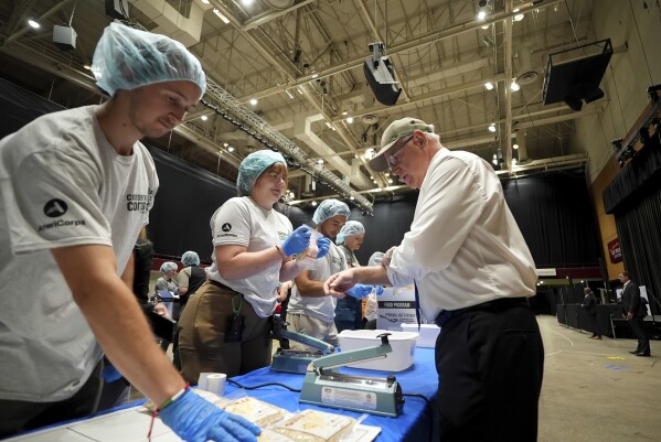 Democratic vice presidential candidate Minnesota Gov. Tim Walz, right, packs meals for local food banks alongside volunteers at Roy Wilkins Auditorium as part of 9/11 National Day of Service, Wednesday, Sept. 11, 2024, in St. Paul, Minn. (Glen Stubbe/Star Tribune via AP)