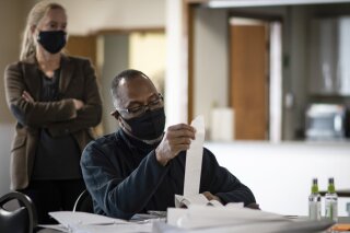 Byron Haskins, an Ingham County Board of Canvasser, reviews tabulator tape collected from Ingham County precincts following the Nov. 3rd election, Wednesday afternoon, Nov. 4, 2020, at the Ingham County Fairgrounds Community Building in Mason, Mich., while attorney Nina Beattie, an observer representing the Democratic Party looks on. (Matthew Dae Smith/Lansing State Journal via AP)