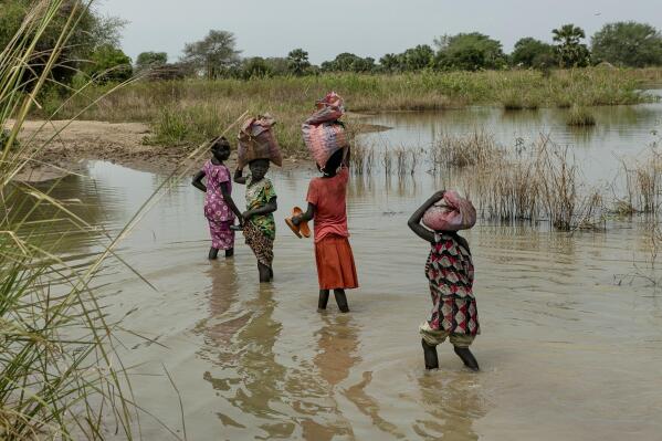 FILE - Children carry bags on their head as they walk the flooded fields near Malualkon in Northern Bahr el Ghazal State, South Sudan, Wednesday, Oct. 20, 2021. (AP Photo/Adrienne Surprenant, File)