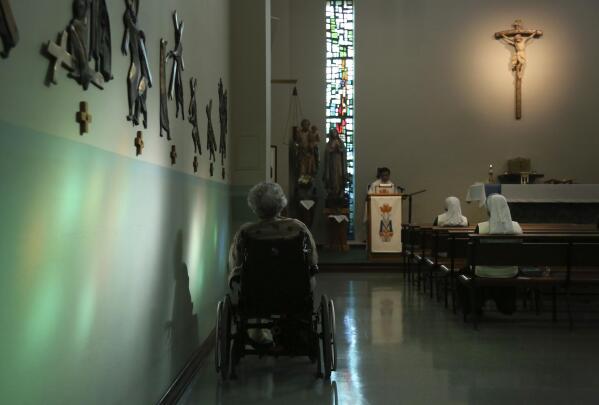 A resident of St. Anne Home sits bathed in sunlight streaming through a stained glass window during morning Mass attended by nuns and residents of the nursing facility in Greensburg, Pa., on Thursday, March 25, 2021. (AP Photo/Jessie Wardarski)