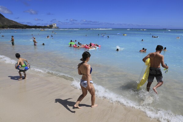 FILE - Beachgoers walk on Waikiki Beach, Thursday, June 23, 2022, in Honolulu. Honolulu police recently got some attention on social media for recommending that beachgoers not leave their valuables unattended and instead put them in a waterproof bag and take them into the ocean.(AP Photo/Marco Garcia, File)