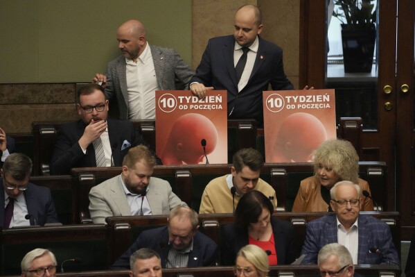 Dariusz Matecki, top right, a conservative lawmaker in the Polish parliament, displays a poster showing a fetus and the words "10th week after conception," during a vote on abortion in Warsaw, Poland, on Friday, April 12, 2024. Polish lawmakers voted Friday to continue work on four proposals that would loosen the law on abortion, a divisive issue in the traditionally Roman Catholic country which has a near-total ban. (AP Photo/Czarek Sokolowski)