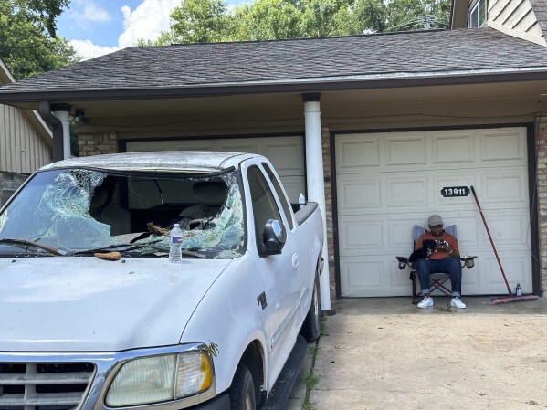 Lisa Reed, a teacher, sits outside her home in the Harris County neighborhood of Cloverleaf near Houston on Sunday, May 19, 2024. Reed said she sat outside because it was too hot to be inside since her home was still without electricity because of last week's storms in the Houston area. The powerful storms knocked down a tree in Reed's front yard, smashing it through the windshield of a family truck. (AP Photo/ Juan A. Lozano)