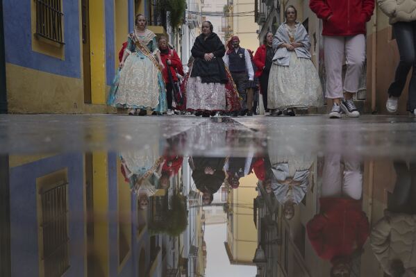 Women dressed in 18th- and 19th-century clothing, known as falleras, are seen reflected in a puddle of rainwater, during the Fallas festival in Valencia, Spain, on Wednesday, March 19, 2025. Five months after deadly floods ravaged Valencia, the Spanish city will host its biggest celebration of the year: Las Fallas. Sculptures were built using wreckage from peoples' homes and lampoon politicians accused of mishandling the catastrophe. (AP Photo/Alberto Saiz)