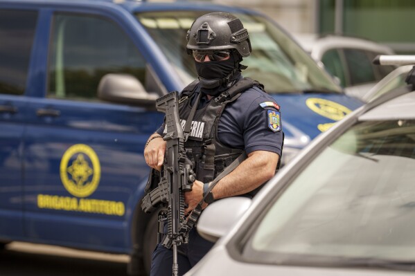 A member of a special unit of the Romanian gendarmerie walks by a van of the anti-terrorist unit of the Romanian Intelligence Service (SRI) outside the apartment block in which the Israeli embassy is located in Bucharest, Romania, Monday, June 3, 2024. A foreign citizen was detained in Romania's capital on Monday after allegedly attacking the entrance of the Israeli Embassy with a Molotov cocktail, causing a small fire but no casualties, local media and police reported. (AP Photo/Vadim Ghirda)