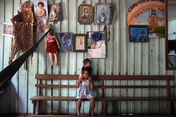 Daughters of fishermen, Tatiana and Andresa, top, sit at their home in San Raimundo settlement in Carauari, Amazonia State, Brazil, Monday, Sept. 5, 2022. Thirty-four families call the area home. (AP Photo/Jorge Saenz)